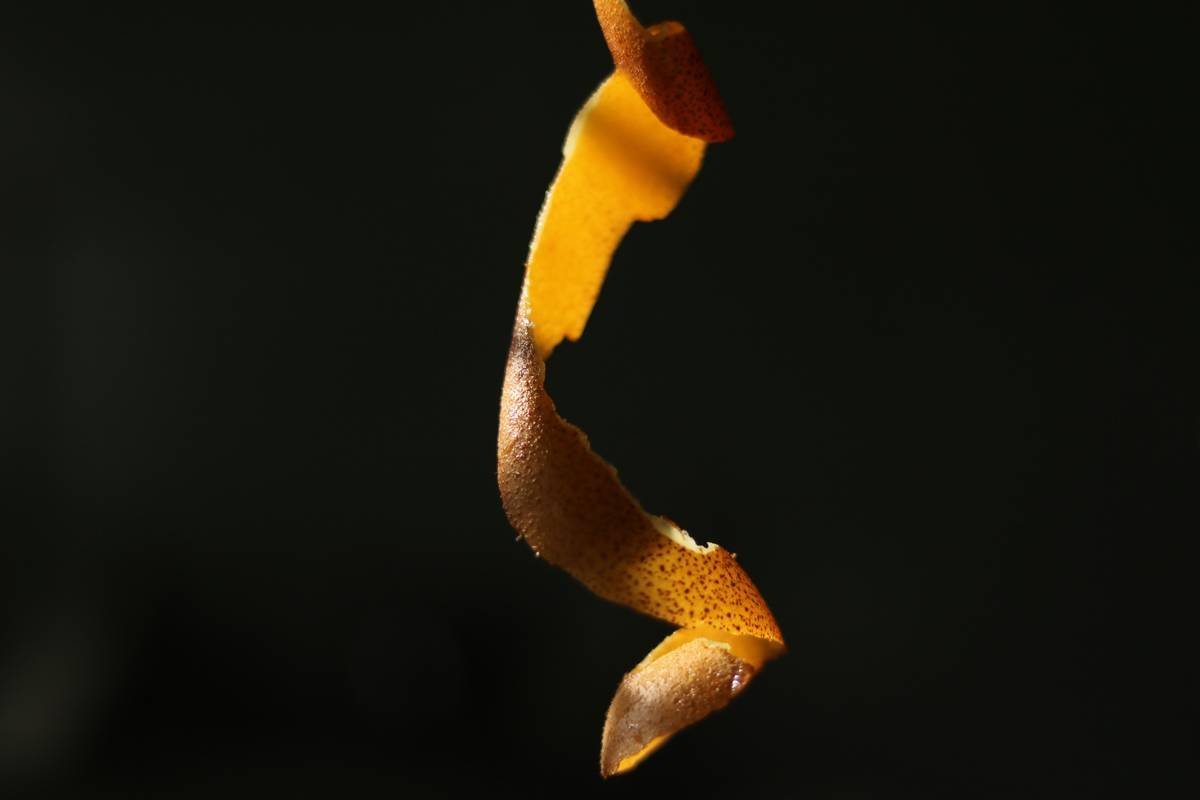 A bottle of organic oil containing citrus peel extract next to fresh citrus fruits.