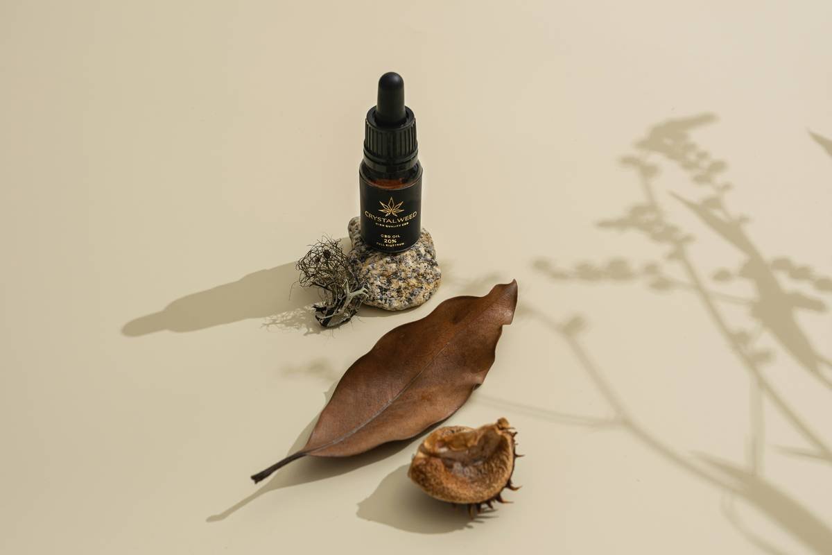 A glass vial of basil essential oil surrounded by fresh basil leaves.